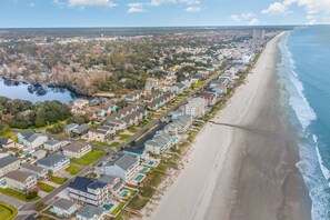 A coastal residential area with houses along the beach, a river, and a clear sky.