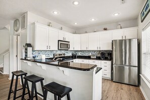 A modern kitchen with white cabinets, a stainless steel refrigerator, a microwave, and a bar area with stools.