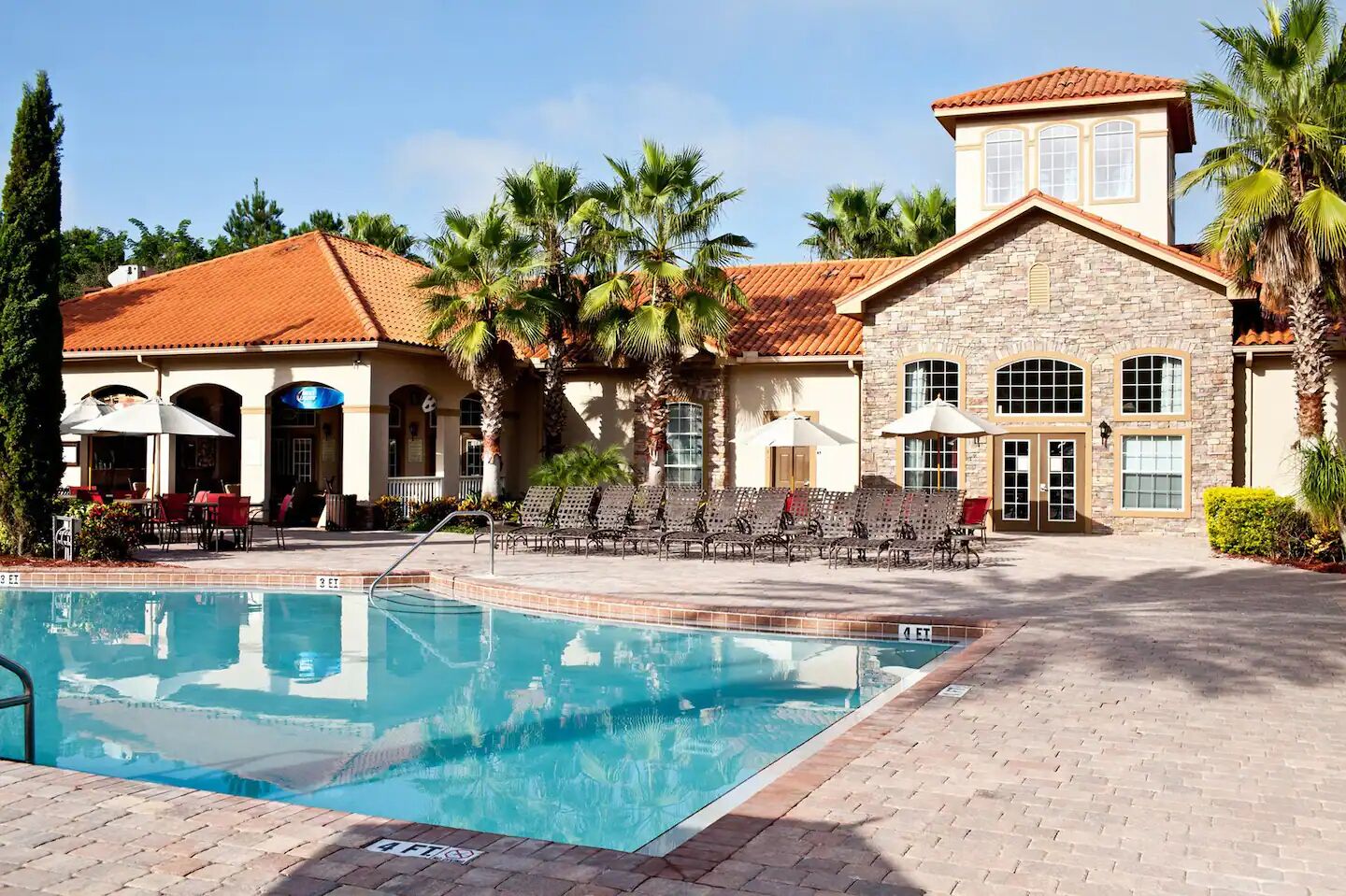 A pool area with lounge chairs and a stone building with arched windows.