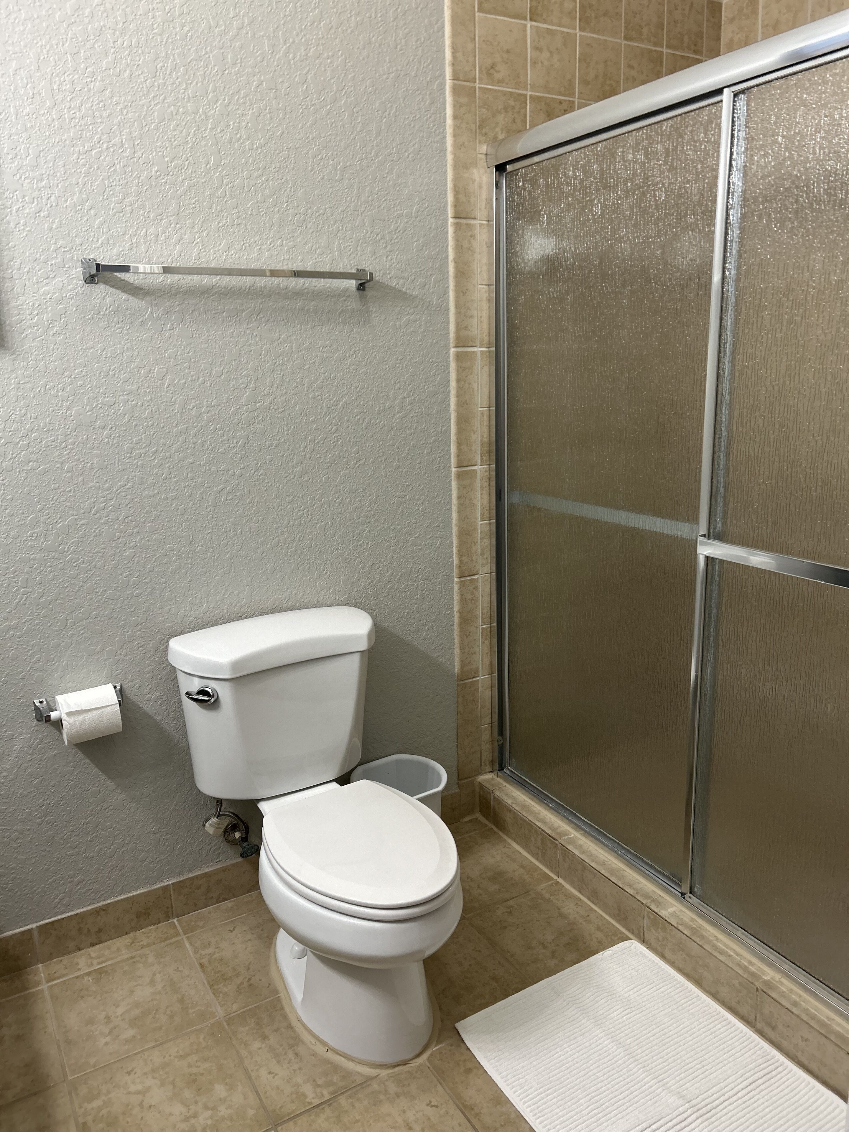 A bathroom with a toilet, a shower with a glass door, and a white floor.