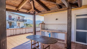 Eine Terrassengruppe im Freien mit einem Holztisch, einer Grillstelle aus Ziegelsteinen und Blick auf eine Berglandschaft.