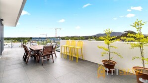 En terrasse med et bord og stole, plantekrukker og udsigt til byggekraner i det fjerne.