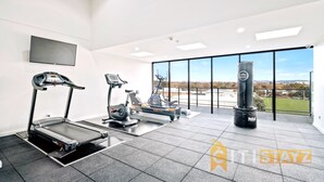 Et moderne fitnesscenter med løbebånd, motionscykel, crosstrainer og boksebold, med et stort vindue der giver udsigt over byen.