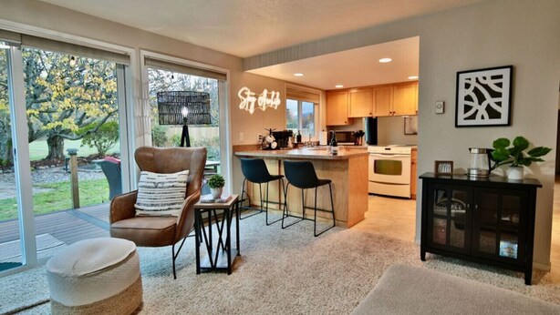 A modern kitchen with a central island, bar stools, and a dining area with a brown leather chair and ottoman. - Family Friendly, wi-fi & hot tub (Port Angeles)