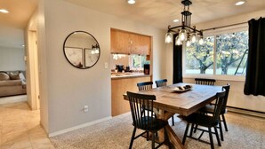 A dining area with a wooden table, black chairs, a chandelier, and a window with a view of trees. - Family Friendly, wi-fi & hot tub (Port Angeles)