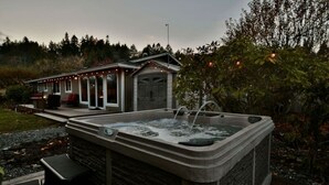 A hot tub with a stone exterior, a covered patio area, and a small building with a garage door in the background. - Family Friendly, wi-fi & hot tub (Port Angeles)