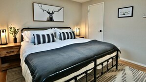 A bedroom with a bed, bedside tables, a nightstand, a wall-mounted picture, and a door. - Family Friendly, wi-fi & hot tub (Port Angeles)