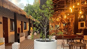 A wooden deck with a large planter, thatched-roof huts, and a dining area with wooden furniture. - Atholhu Residence  (Fehendhoo)