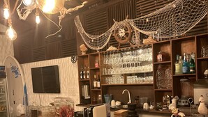 A bar area with a wooden counter, bar stools, a menu sign, and a decorative rope canopy. - Atholhu Residence  (Fehendhoo)