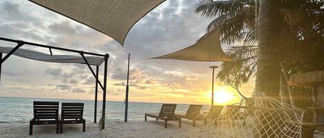 A beach with a hammock, lounge chairs, and a shaded area.