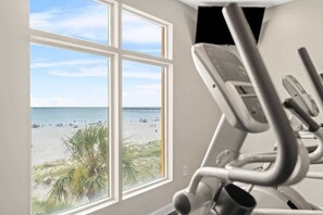 A gym with a view of a beach and pier through a large window.