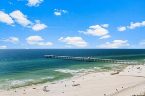 A beach with a pier extending into the ocean, sandy shore, and clear skies.