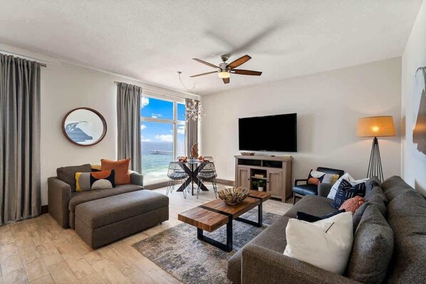 A living room with a sofa, a coffee table, a TV, and a view of the sea.