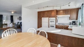 Une cuisine moderne avec des meubles en bois, un plan de travail blanc et un coin repas comprenant une table et des chaises en bois.