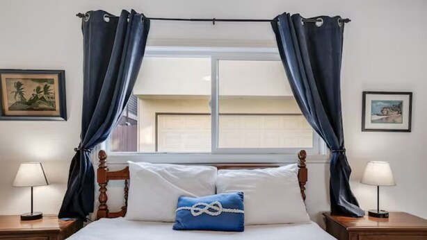 Un lit bien fait, avec un oreiller bleu, une tête de lit en bois et deux tables de chevet dotées de lampes.