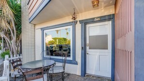 Un espace extérieur aménagé avec une table et des chaises, une porte blanche et une fenêtre donnant sur la rue.