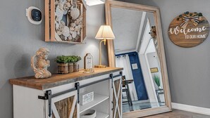 Un interior moderno con una consola de madera, objetos decorativos y un espejo que refleja un pasillo.