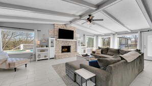 Un salón amplio con chimenea de piedra, un sofá grande de color gris y un ventilador de techo.