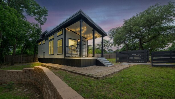 Una casa moderna con un porche cubierto, ventanas amplias y un muro de contención de piedra.