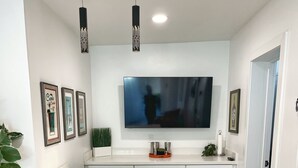 Una cucina moderna con una grande isola, due sgabelli da bar, una TV a schermo piatto e quadri appesi al muro.
