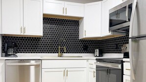 Une cuisine moderne avec des meubles blancs, un pare-feu noir et blanc, des appareils en acier inoxydable et un plancher en bois.