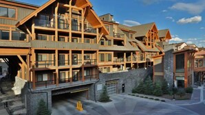 Un bâtiment à étages, de style chalet, avec une façade en pierre, de nombreux balcons et un espace de stationnement couvert.