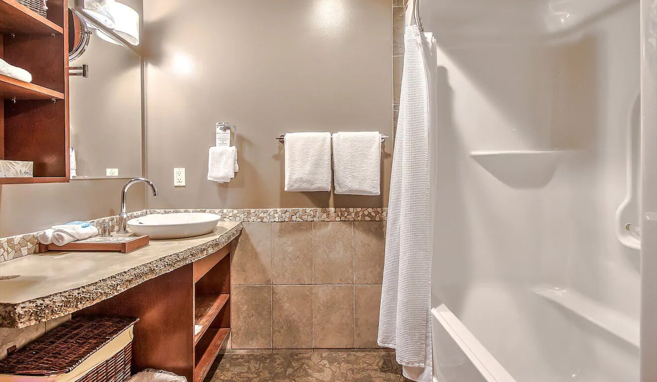 Un baño con lavamanos, espejo, toallero y ducha.