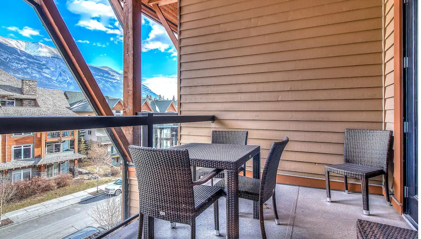 A balcony with wicker furniture, a view of a mountain, and a building with wooden siding.