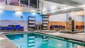 Une piscine intérieure avec des chaises longues bleues, des étagères remplies de serviettes et un mur en pierre.