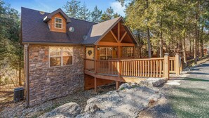 A stone cabin with a wooden deck, surrounded by trees.