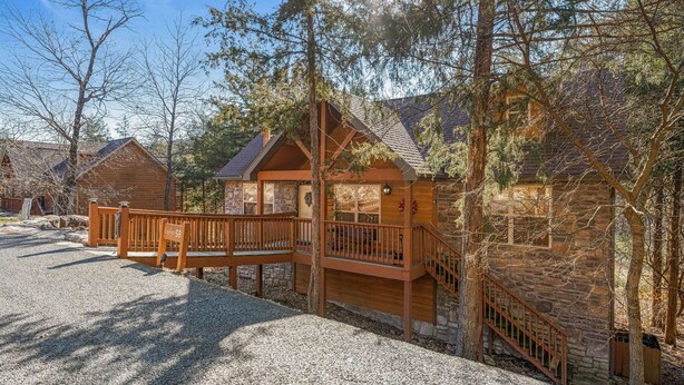 A rustic cabin with a stone exterior, wooden deck, and a staircase leading to a balcony.