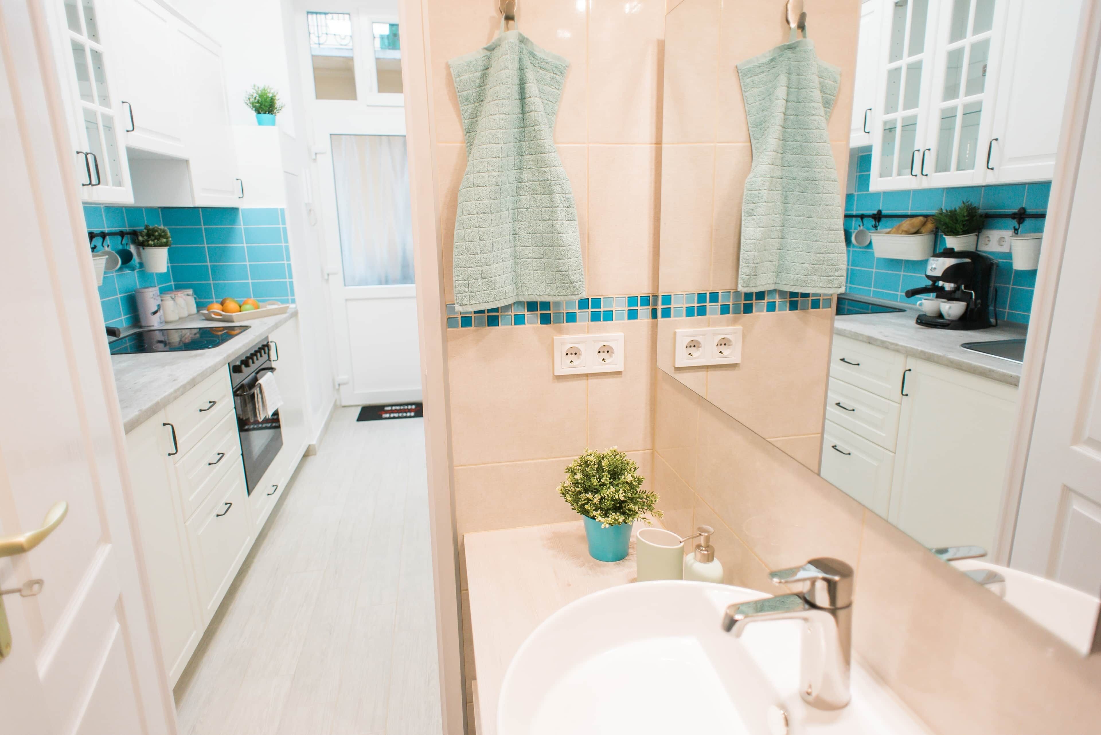 A modern kitchen with white cabinets, a stove, and a sink. There are two towels hanging on the wall, and a small plant on the counter.