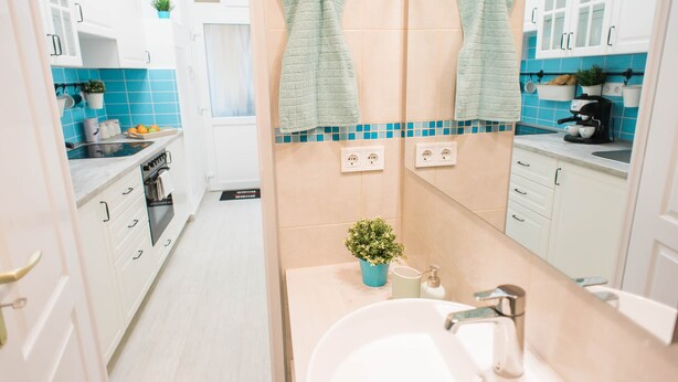 Una cocina moderna con gabinetes blancos, una estufa y un lavamanos. Hay dos toallas colgadas en la pared y una pequeña planta en la encimera.