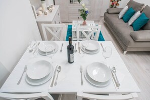 A dining table set for two with white plates, silverware, and a bottle of wine.