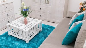 Una habitación con un aparador blanco, un sofá blanco con cojines turquesa y una pequeña mesa blanca con un florero.
