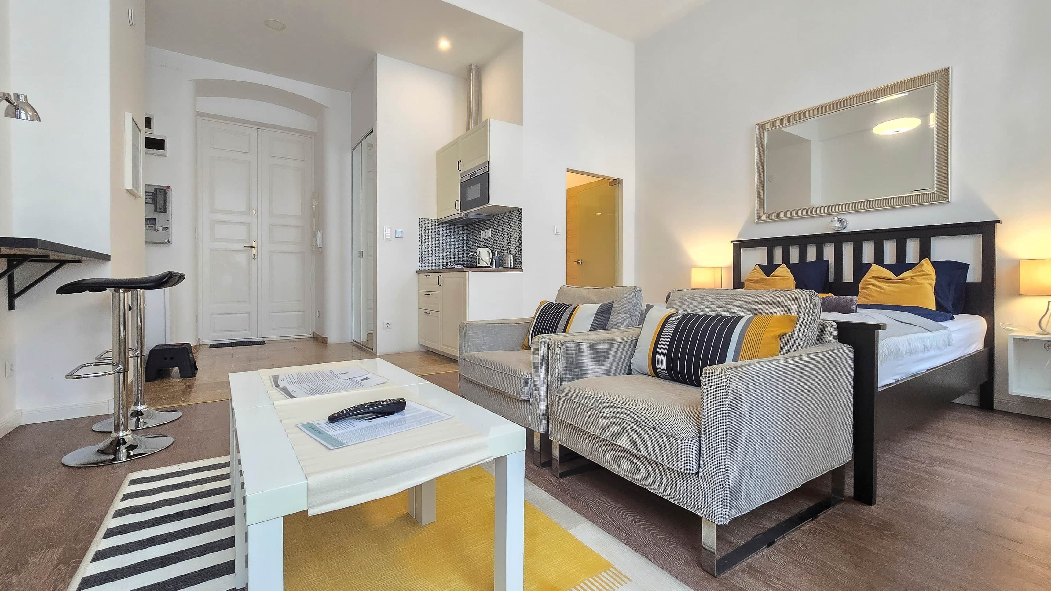 Una sala de estar moderna con sofá, una mesa de centro, televisor y una cocina visible a través de una puerta abierta.