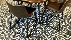 Un coin repas comprenant une table ronde en bois, quatre chaises, un tapis à motifs, une bibliothèque et un réfrigérateur en acier inoxydable.