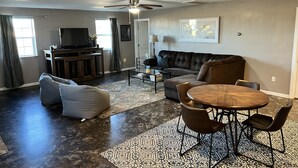 Un salon spacieux avec un canapé d’angle, une table basse et un coin repas avec des chaises.