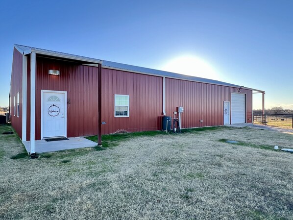 A red metal building with a white door and a welcome sign, a small window, and a garage door. - Barndominium on Gorgeous Ranch! (Washington)