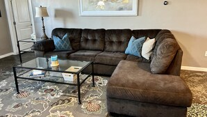 Un salon avec un canapé marron, une table basse en verre et un tapis à motifs.