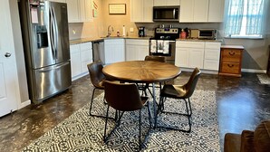 Une cuisine moderne avec des meubles blancs, des appareils en acier inoxydable, une table ronde en bois et des carreaux de sol à motifs.