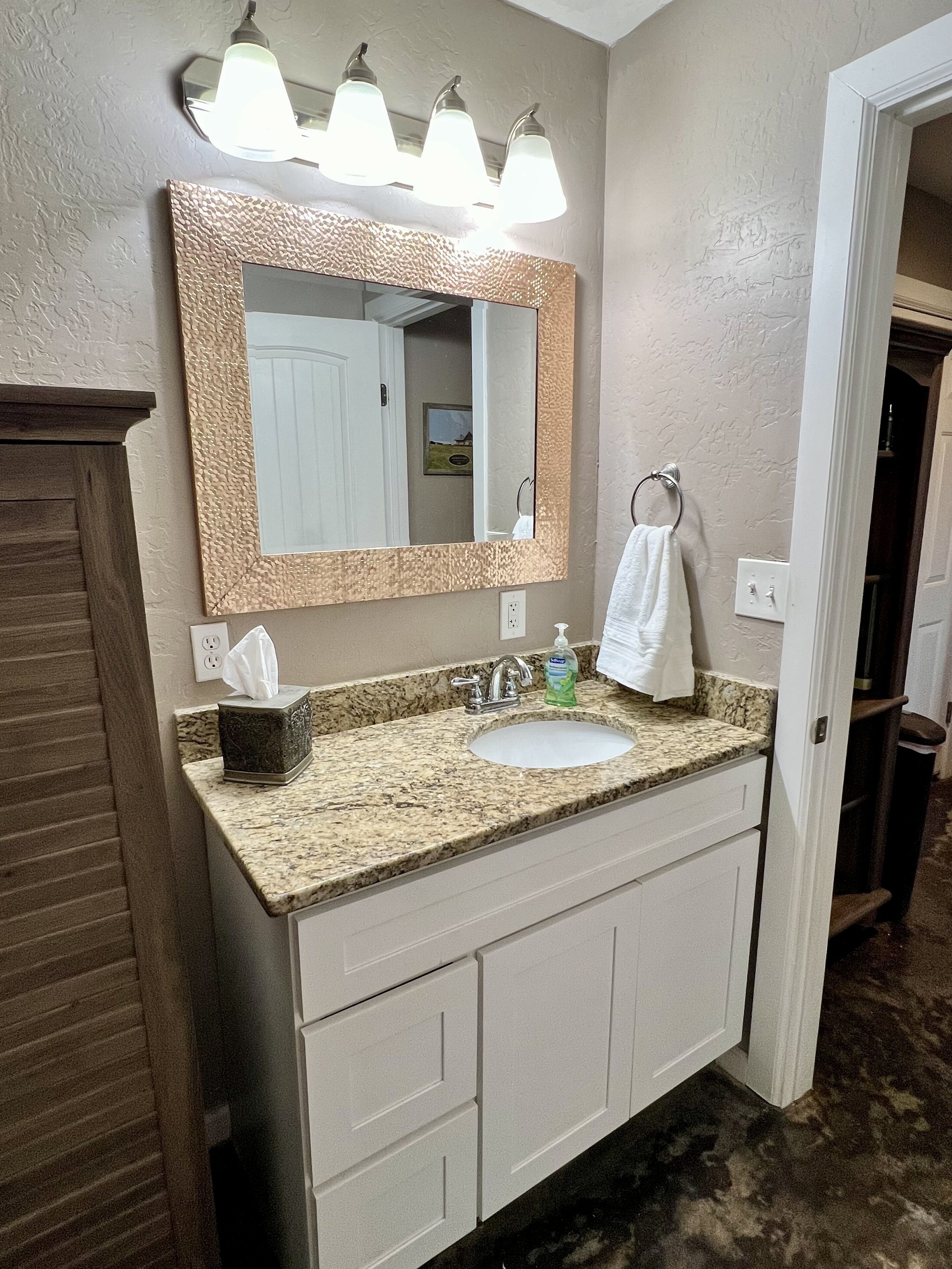 A bathroom with a granite countertop sink, a large mirror with a textured frame, and a towel ring.