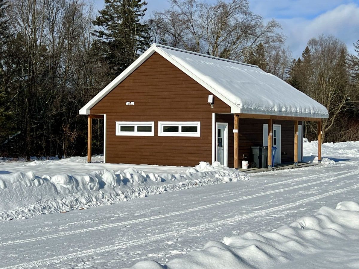 Une cabane en bois avec un toit enneigé, un garage et une véranda couverte.