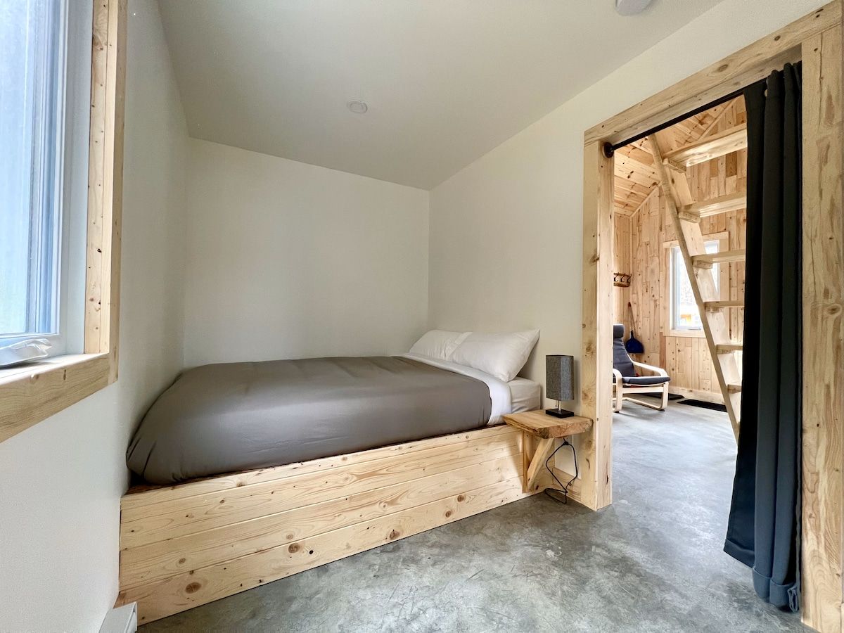 Une chambre à coucher comprenant un lit, une table de chevet, une chaise et une échelle en bois menant à un niveau supérieur.