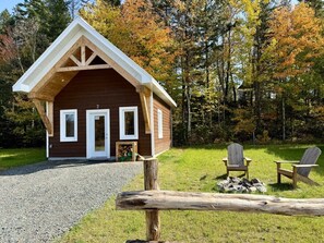 A cabin with a pitched roof, a gravel driveway, and two Adirondack chairs in front. - Mini-Chalet #2 – Near the River (Saint-Gabriel-de-Valcartier)
