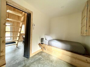 Una habitación compacta con cama tipo altillo, una mesita de noche pequeña y una escalera que lleva a un nivel superior.