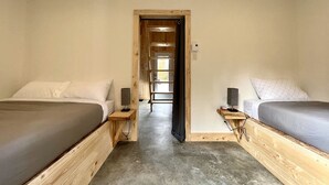 A room with two beds, a wooden floor, a door leading to a corridor, and a light switch on the wall. - Mini-Chalet #2 – Near the River (Saint-Gabriel-de-Valcartier)