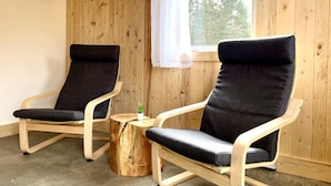 Dos sillones de descanso negros con estructura de madera en una habitación con paredes de madera y una ventana.