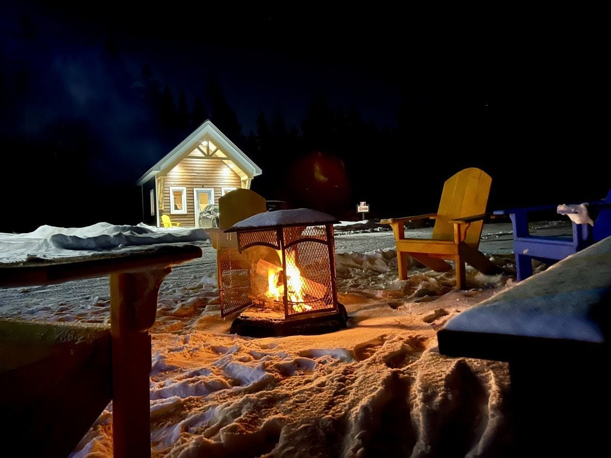 Eine Holzjagdhaus mit einem Feuerkorb im Vordergrund, einem Stuhl und einem Tisch im Hintergrund.