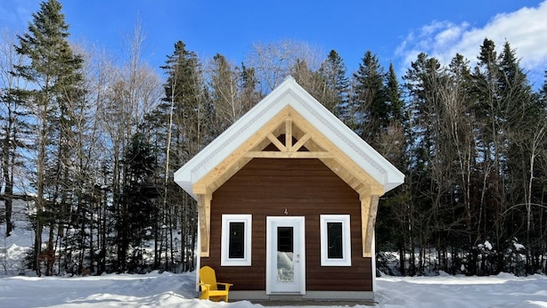 A wooden cabin with a white door and windows, surrounded by snow and trees. - Mini-Chalet #4 – Near the River (Saint-Gabriel-de-Valcartier)
